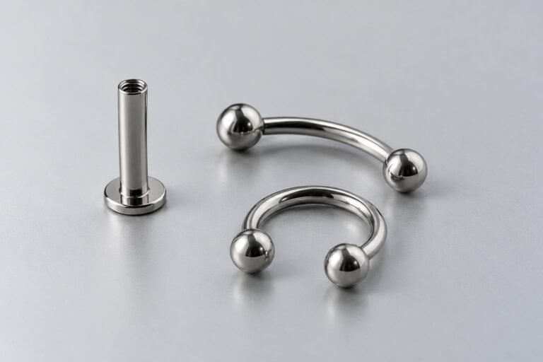 Piercingsieraden met een zilverkleurige uitstraling: een labret met platte achterkant, een gebogen barbell en een ronde ring.