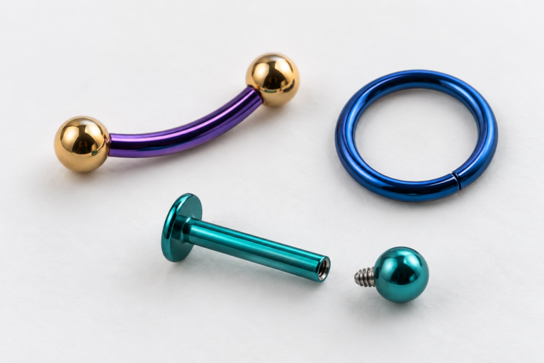 Drie piercingsieraden op een witte ondergrond: een paarse gebogen staaf, een blauwe ring en een turquoise labret met losse bol