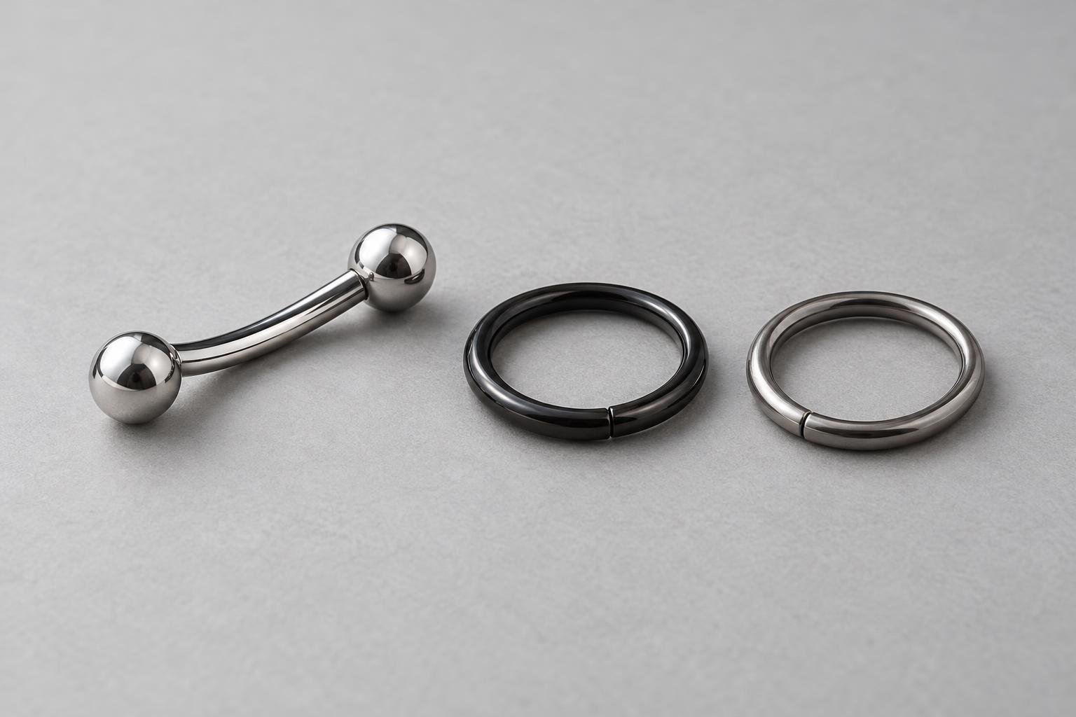 Un bilanciere curvo lucido, un anello nero e un anello metallico argentato su fondo chiaro