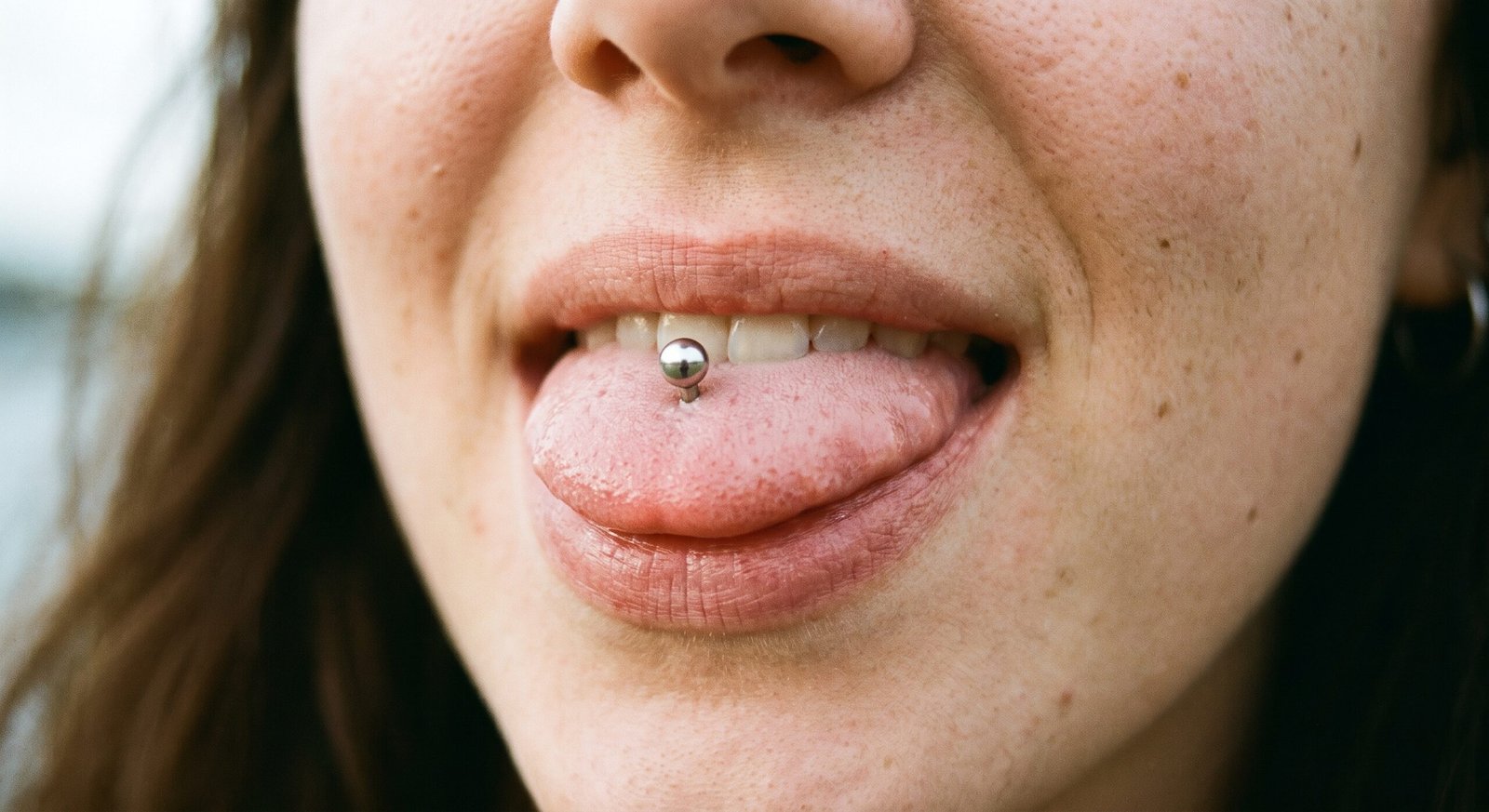 Piercing linguale tradizionale verticale con terminale a sfera visibile sulla lingua protrusa