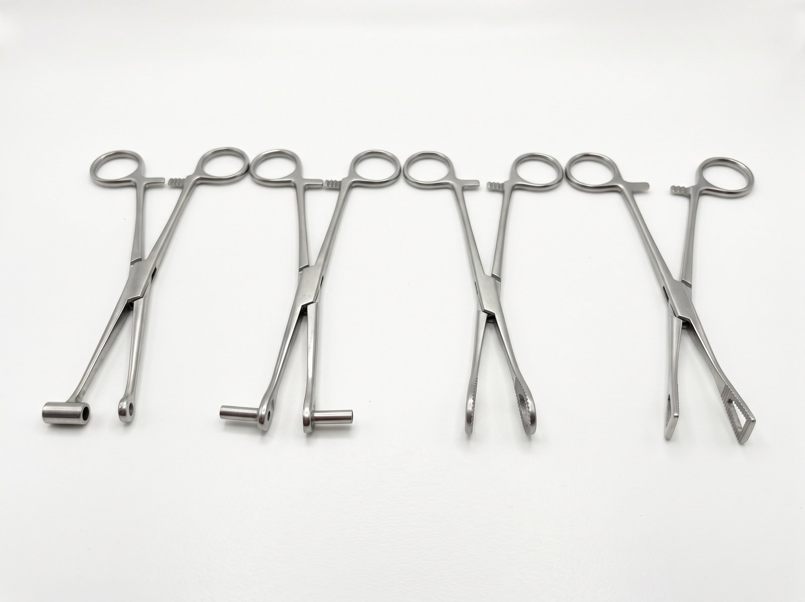 Pinze per body piercing con diverse forme delle estremità, disposte su fondo bianco.